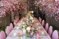 a fantastic blooming wedding reception space with pink blooming branches over it, a chic tablescape with pink plates, glasses and blooms and gold touches