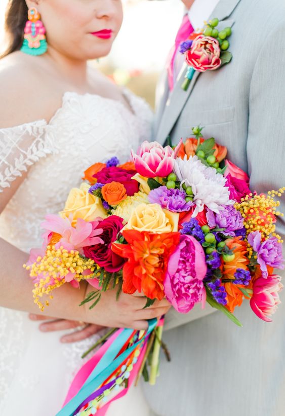 a fantastic colorful wedding bouquet of yellow, red, purple, hot pink blooms, berries and colorful ribbon is amazing