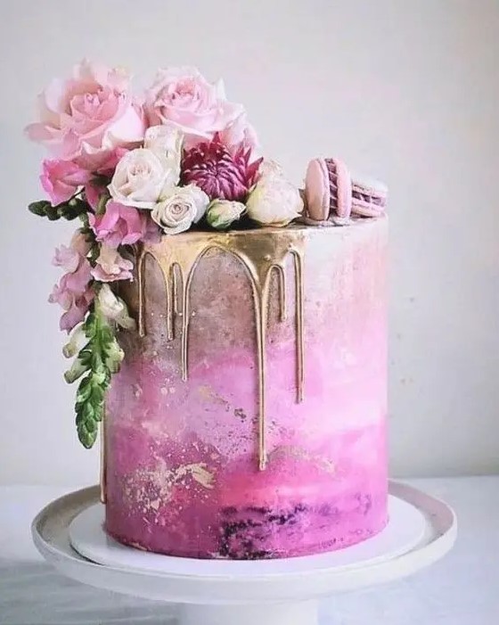 a fantastic hot pink wedding cake with an ombre effect, gold drip, pink macarons and pink blooms on top for a glam wedding