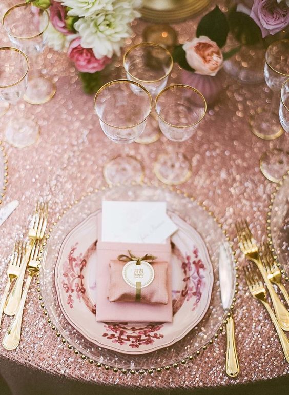 a glam blush and gold wedding tablescape with neutral and pink blooms, a pink plate and napkin, gold cutlery and gold-rimmed glasses