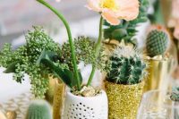 a glam wedding centerpiece of potted blooms, cacti and greenery in white and glitter planters