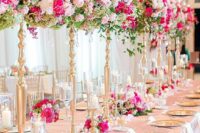a glam wedding tablescape with a pink tablecloth and neutral napkins, tall light and hot pink wedding centerpieces and matching arrangements on the tables, gold plates and stands
