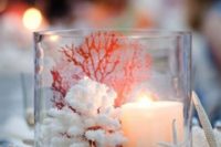 a large glass with sand, corals, a star fish, a candle and seashells plus starfish all around for a beach wedding