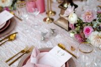 a lovely and sweet wedding tablescape with a blush sequin tablecloth and pink napkins and plates, hot pink candles and pink blooms, gold cutlery