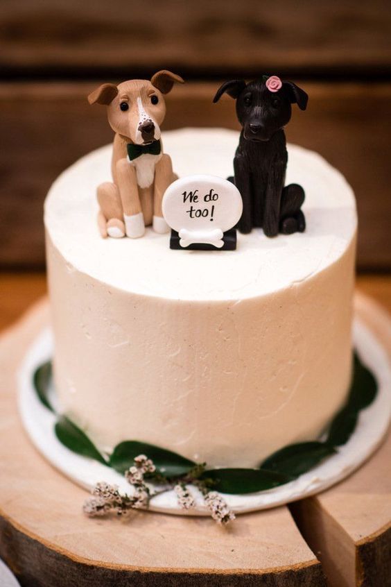a lovely white wedding cake decorated with leaves and topped with dogs plus a sign is a cute idea for a dog-loving couple