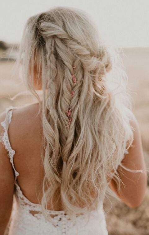 a messy boho wedding half updo with multiple twists, braids and waves and with some blooms tucked into the hair