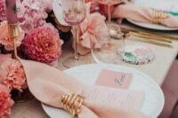 a modern and beautiful pink and gold wedding tablescape with pink florals and candles, blush napkins and gold cutlery, pink glasses
