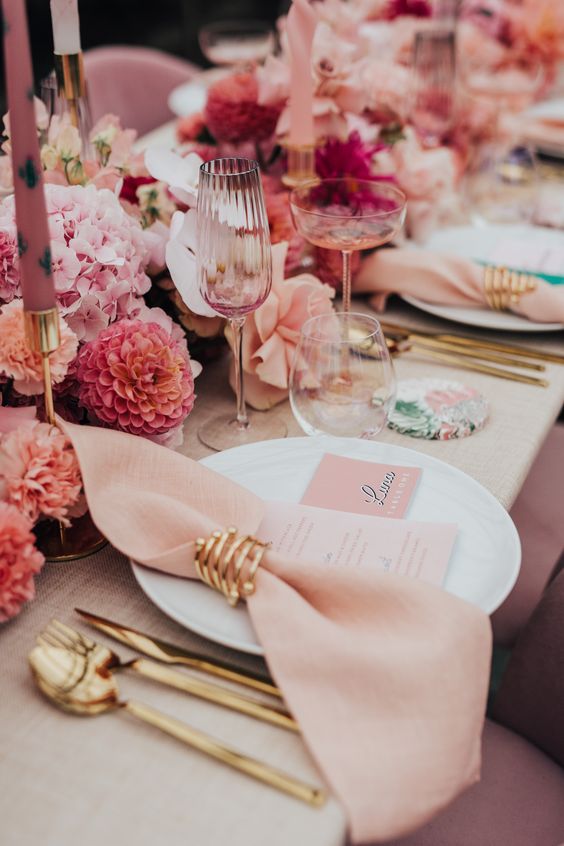 a modern and beautiful pink and gold wedding tablescape with pink florals and candles, blush napkins and gold cutlery, pink glasses