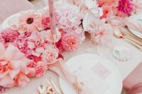 a modern bright wedding tablescape with a lush pink floral table runner, pink napkisn and gold cutlery, blush candles is chic