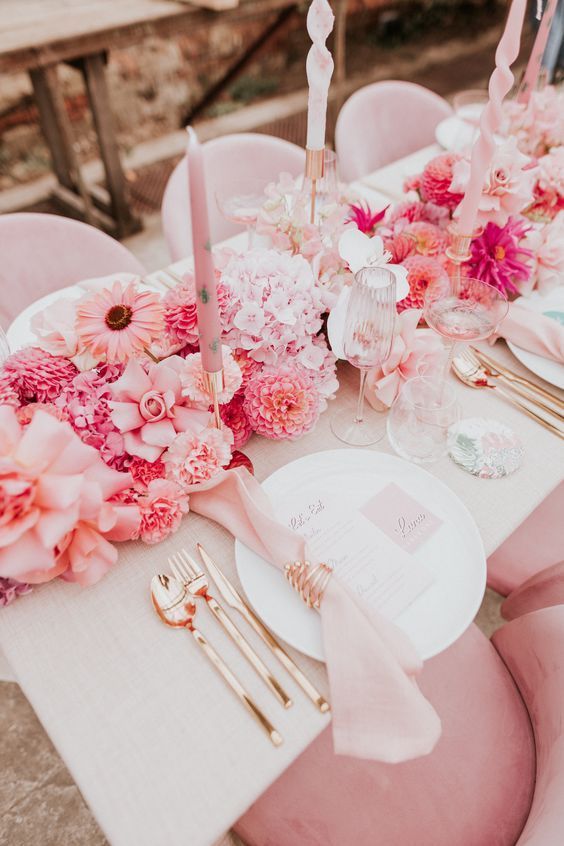 a modern bright wedding tablescape with a lush pink floral table runner, pink napkisn and gold cutlery, blush candles is chic