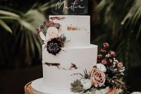 a naked wedding cake decorated with neutral and dark blooms, greenery and thistles, an acrylic and calligraphy cake topper for a modern wedding