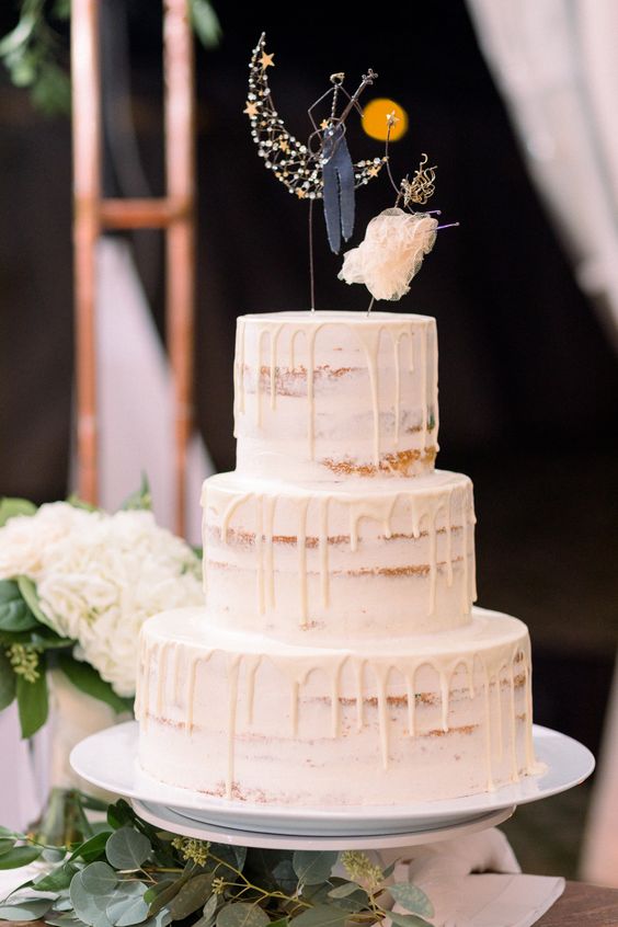 a naked wedding cake with drip and some lovely cake toppers showing off a bride and a groom at the moon