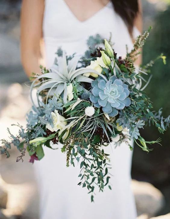 a neutral wedding centerpiece of greenery, succulents, airplants, thistles and white blooms is romantic
