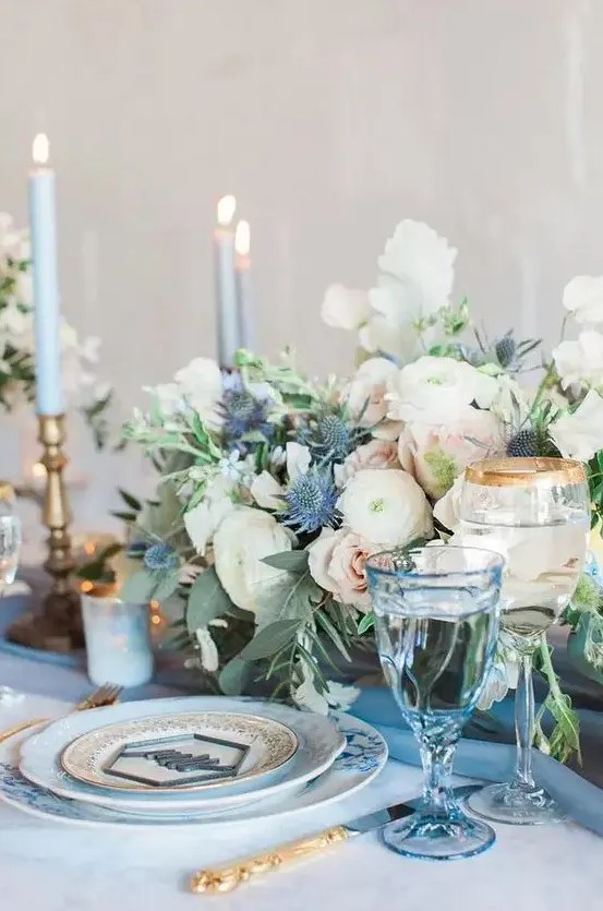 a pastel wedding tablescape with a pale blue table and glasses, blue candles, pastel and white blooms and blue thistles