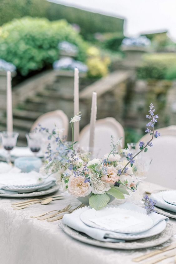 a refined garden wedding tablescape with pale blue napkins, peachy and blue floral centerpieces, grey candles and gold cutlery