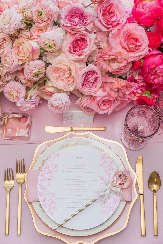 a refined pink and gold wedding tablescape with lush ombre florals, a pink tablecloth and napkin, a gold-rimmed charger and gold cutlery