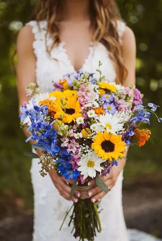 a relaxed and colorful wildflower wedding bouquet with sunflowers, daisies, blue and pink blooms and baby's breath