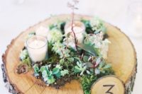 a rustic wedding centerpiece with moss, succulents, candles and with a table number for coziness and a natural feel