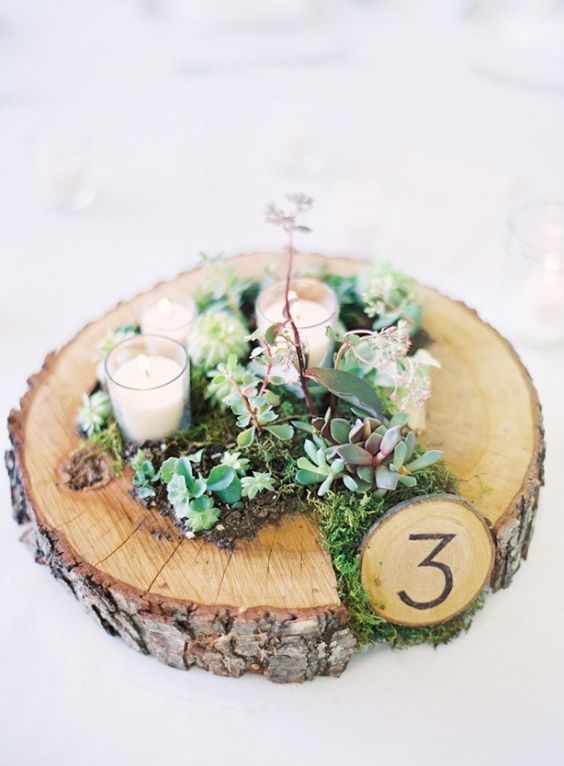 a rustic wedding centerpiece with moss, succulents, candles and with a table number for coziness and a natural feel