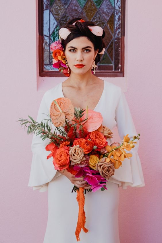 a saturated wedding bouquet of red, coffee colored, yellow and pink blooms and greenery and long orange ribbon for a super bold wedding in summer