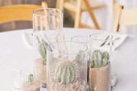 a simple desert wedding centerpiece of cacti planted in tall glasses and candles is a stylish idea