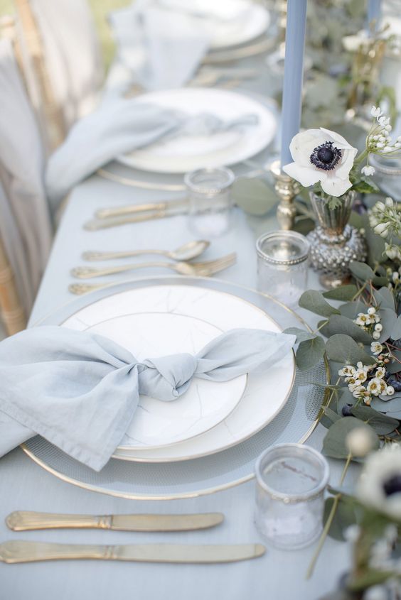 a sophisticated wedding tablescape with a pale blue tablecloth and napkins, greenery and white anemones, blue candles