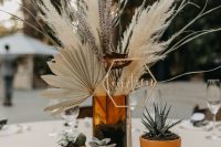 a stylish boho wedding centerpiece of dried fronds, pampas grass and herbs, potted succulents and candles