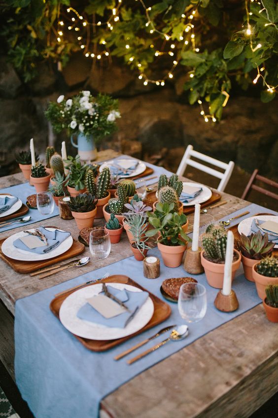 a stylish wedding tablescape with a potted succulent and greenery table runner and candles plus touches of wood