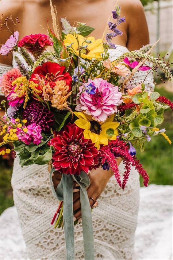 a sumptuous color wedding bouquet of pink, burgundy and purple dahlias, yellow blooms, purple ones and greenery plus long green ribbon