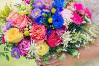 a super bold and colorful summer wedding bouquet of purple, yellow, pink and hot pink blooms, blue ones and some greenery and herbs
