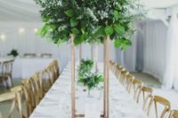 a tall greenery centerpiece of various types of eucalyptus and some foliage on a geometric copper stand