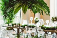 a tall tropical wedding centerpiece with large tropical leaves is a cool and fresh idea for a tropical wedding