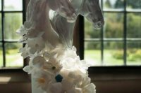 a unique white wedding cake inspired by horses, with sugar blooms and white horse head on top is a fantastic idea
