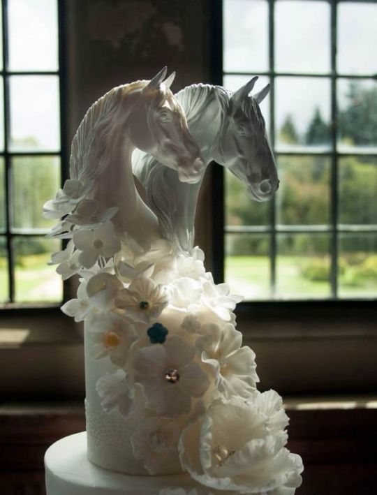 a unique white wedding cake inspired by horses, with sugar blooms and white horse head on top is a fantastic idea