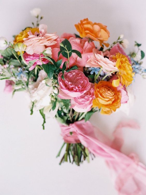 a vivacious summer wedding bouquet of pink and blush peony roses, yellow ranunculus, greenery and pink ribbon