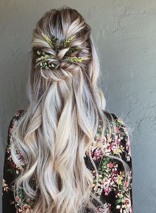 a wavy half updo with a volume on top, twisted greenery decorated element and waves down
