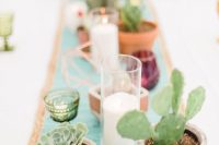 a wedding table runner of candles in glasses, pots with cacti and succulents and copper himmeli