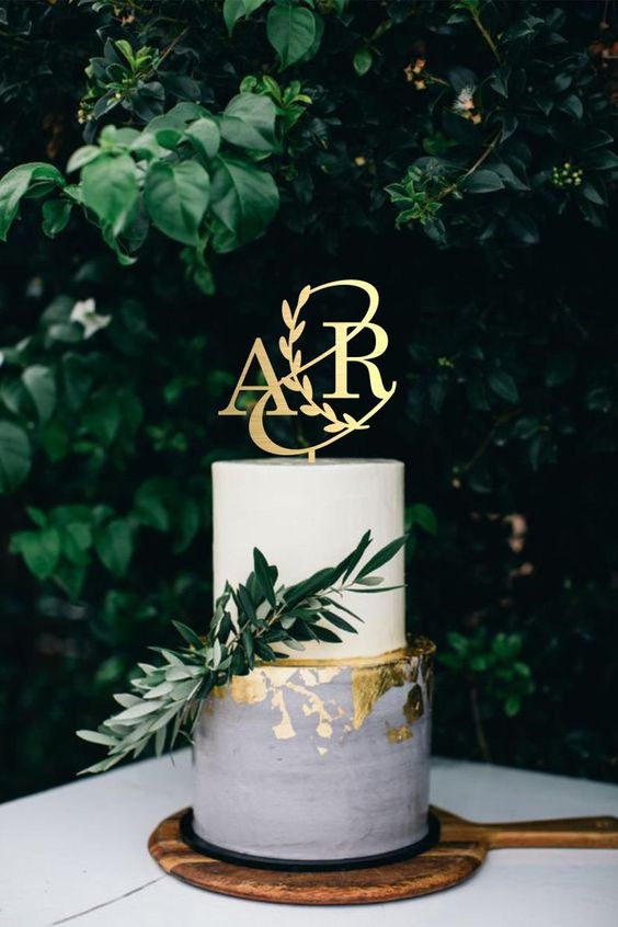 a white and grey wedding cake with gold foil, with greenery and a gold monogram cake topper is a chic and stylish solution
