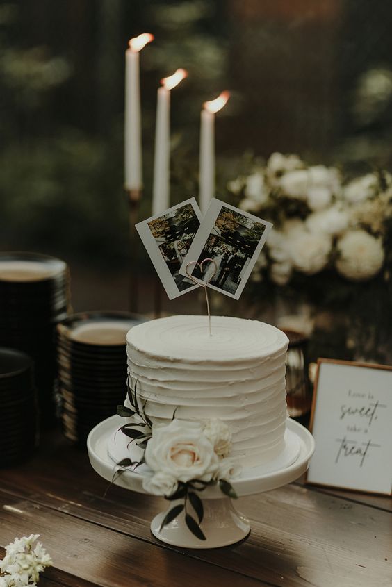 a white buttercream wedding cake decorated with a white rose and greenery and a couple of photos as cake toppers is a great idea