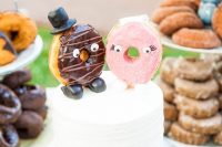 a white buttercream wedding cake topped with glazed donuts dressed up like a marrying couple look very cute and nice