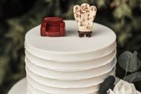 a white buttercream wedding cake topped with two different chairs symbolizing the marrying couple