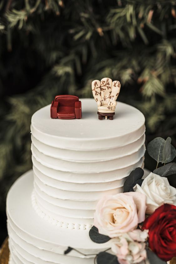 a white buttercream wedding cake topped with two different chairs symbolizing the marrying couple