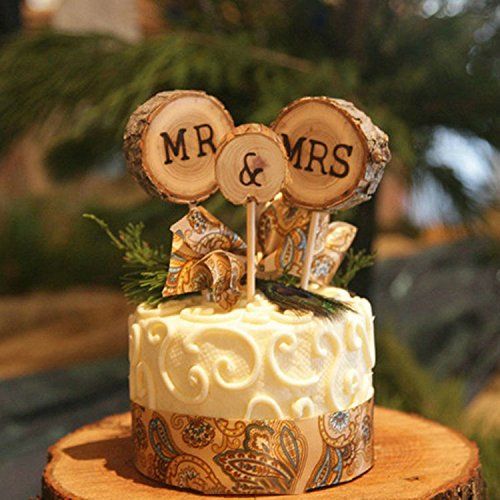 a white patterned wedding cake with a bright ribbon, greenery and tree slice cake toppers with wood burning