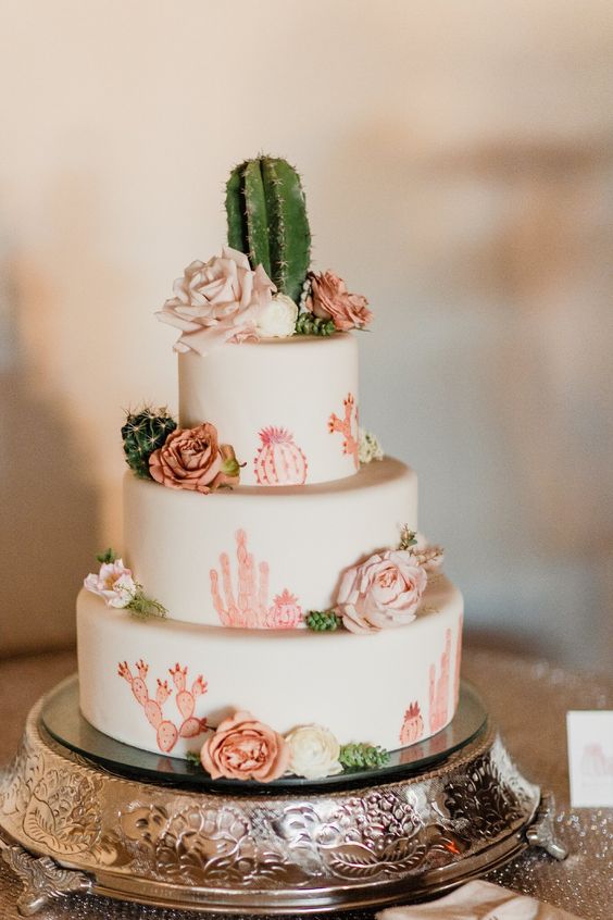 a white wedding cake with pink cactus painted, blush blooms and real cacti for decor