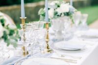 an elegant pale blue and white wedding tablescape with pale blue menus, candles and a table runner, white blooms and gold touches
