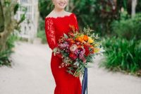 an off the shoulder red mermaid wedding dress of lace, with a small train, a colorful wedding bouquet with greenery and ribbon