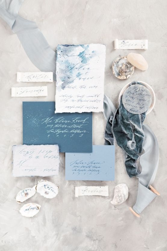 a beach wedding invitation suite done with a navy envelope, a light blue one, white pieces with a raw edge, blue ribbon and oysters