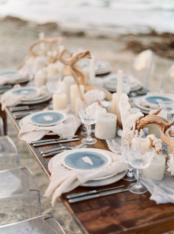 a beach wedding tablescape with a fabric runner and napkins, blue plates, candles and driftwood looks natural and beautiful