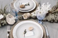 a beach wedding tablescape with a grey tablecloth, gilded placemats, neutral porcelain, pebbles, seashells, corals and air plants