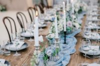 a beautiful light blue summer wedding table with a runner, white candles and pastel blooms and grey chargers